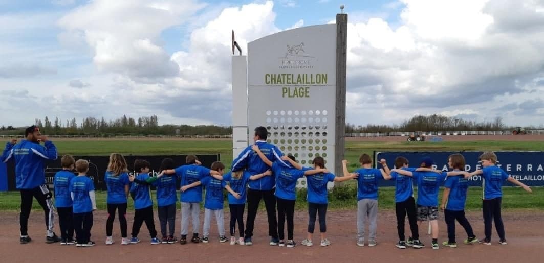 Les jeunes athlètes du CAC en t-shirt bleu devant le panneau de l'hippodrome de Châtelaillon-Plage